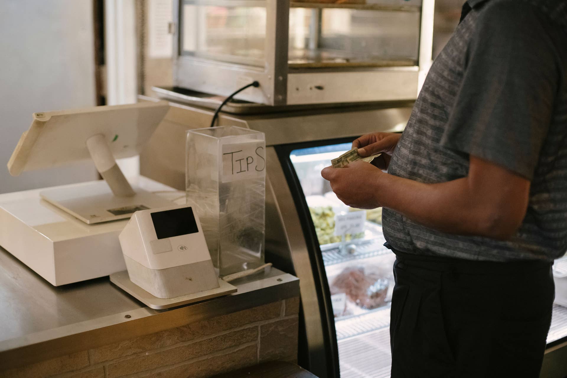 Close-up of a person making a cash payment at a store counter with a digital register, Photo Credit: Tim Samuel/Pexels