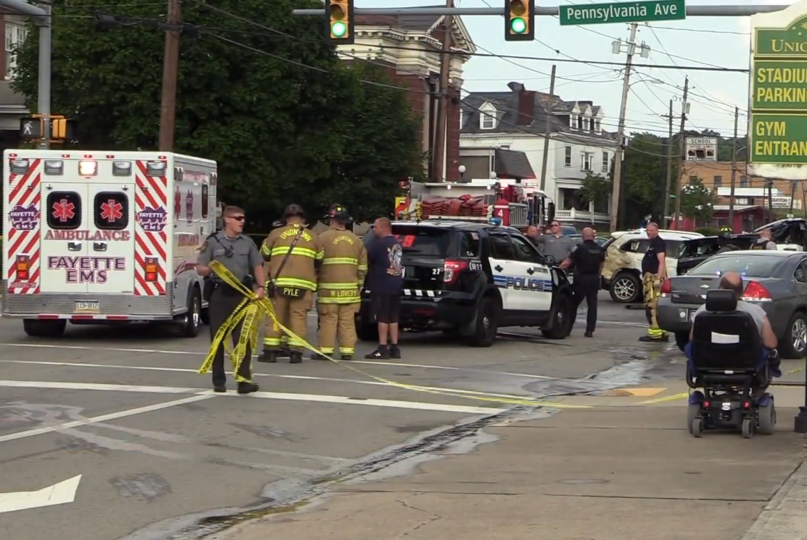 An emergency response scene at an intersection with a Fayette EMS ambulance, police vehicle, and firefighters, Photo Credit: CBS Sunday Morning/Youtube