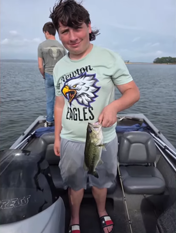 Beau Vayon holding a largemouth bass fish while standing on a fishing boat, Photo Credit: 12NewsNow/Youtube