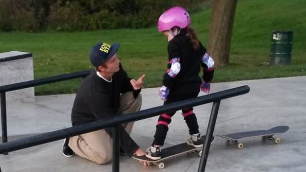teen helps young girl learn to skateboard