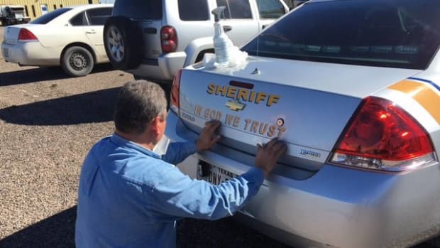 an Ector County Sheriff adds the 'In God We Trust' decal to a patrol car