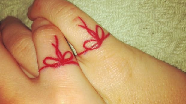 hand with red string tattoo around finger
