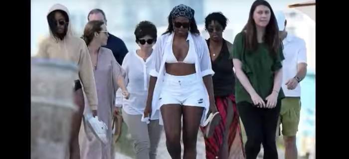 Michelle Obama walking on the beach with her daughter and a group of people behind her, Photo Credit: Youtube