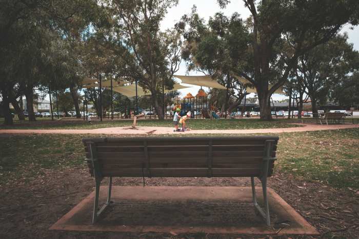 Wooden bench in park with kids playing, Photo Credit: Pexels