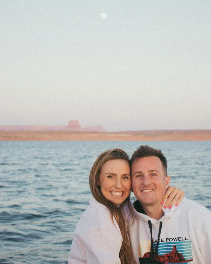 Amanda Cooper holding her husband smiling in front of a body of water, Photo Credit: amandak_cooper/Instagram