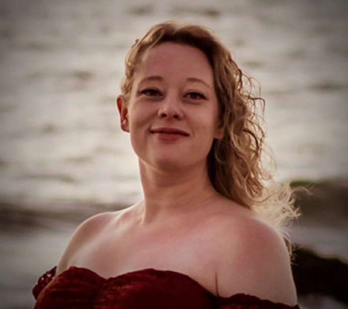 Renee Nicole Good wearing a red dress with curly long hair, Photo Credit: Dr Louise Raw/X