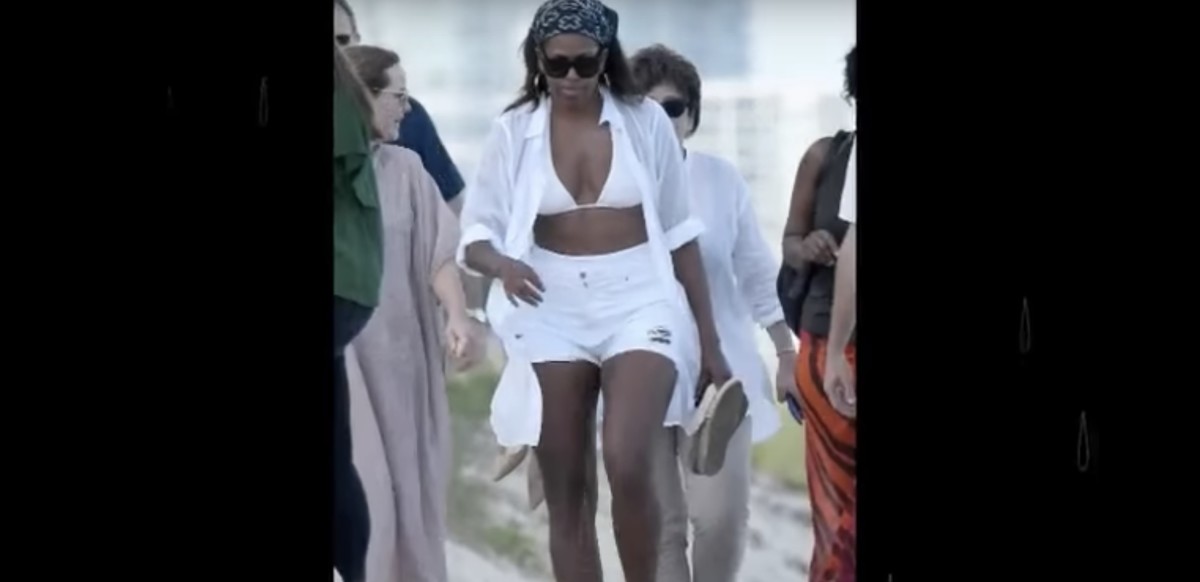 Michelle Obama walking on the beach with her daughter and a group of people behind her, Photo Credit: Youtube