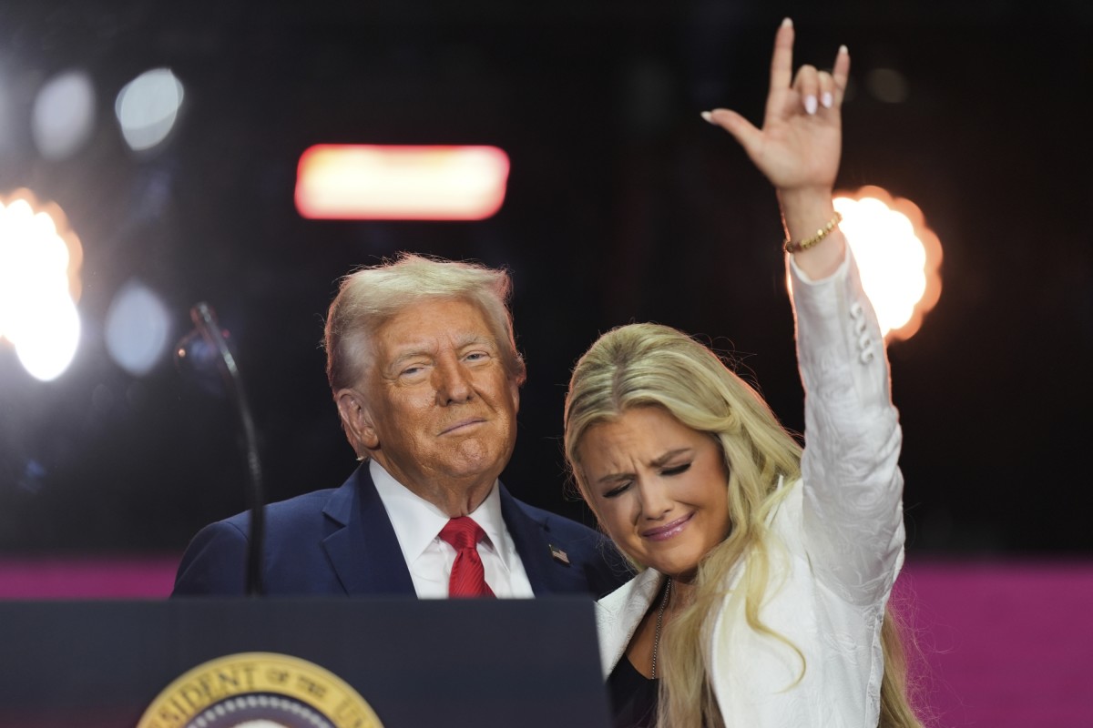 President Donald Trump standing with Erika Kirk who makes a hand gesture during Charlie Kirk's memorial, Photo Credit: Spitfire/X