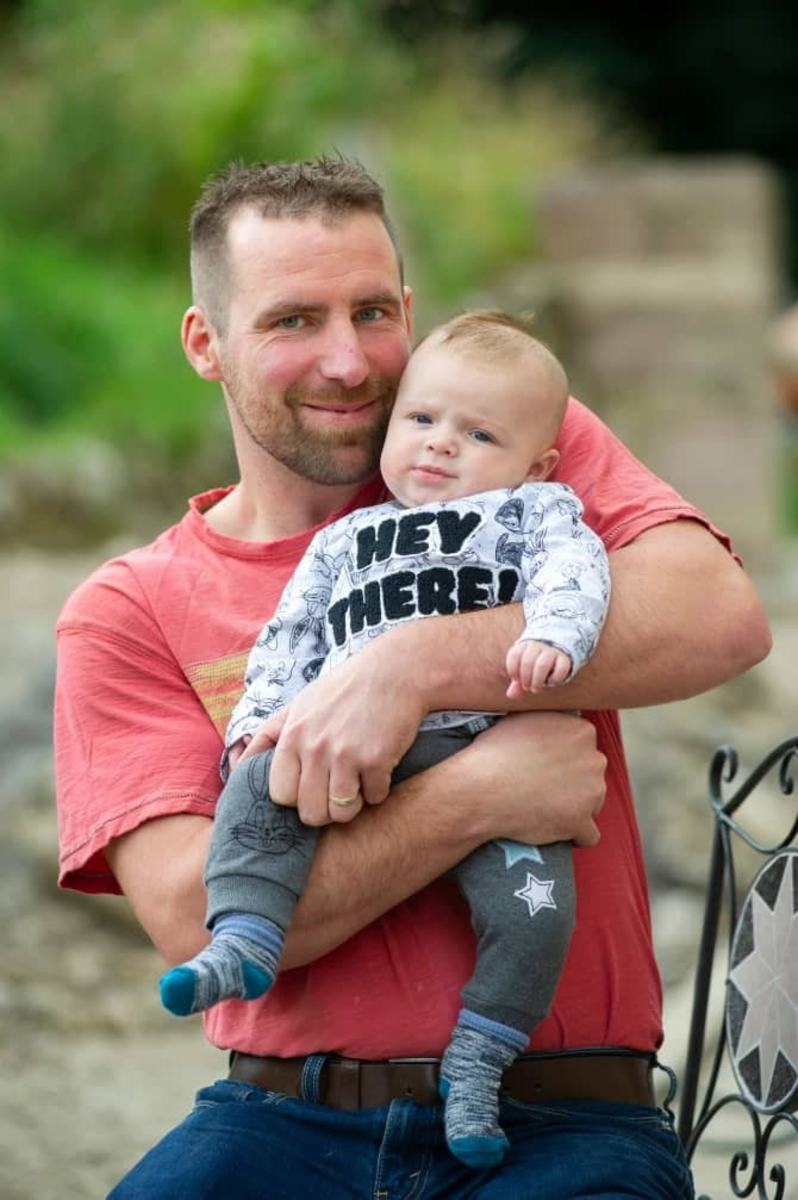 Dan Sheldon holding his baby son Lucifer in an outdoor area, Photo Credit: hurumacharles/Instagram